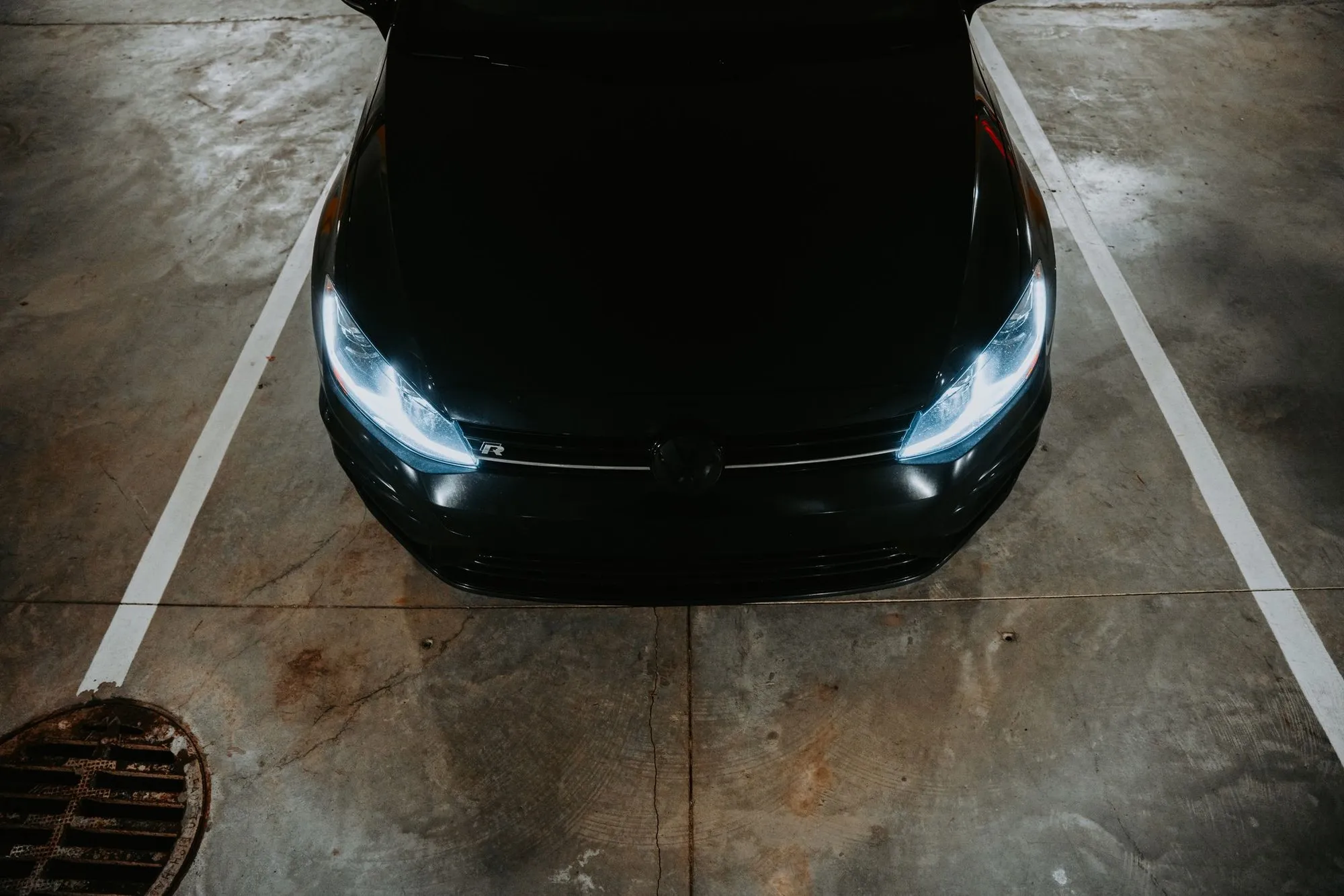 A dark car photographed from directly above, parked between white bay lines