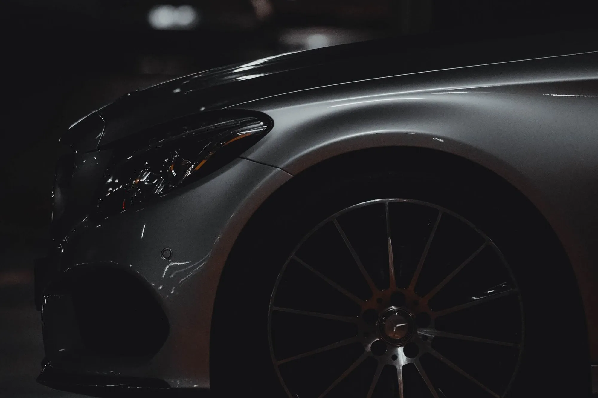 Close detail of a dark car front wing and wheel under low light