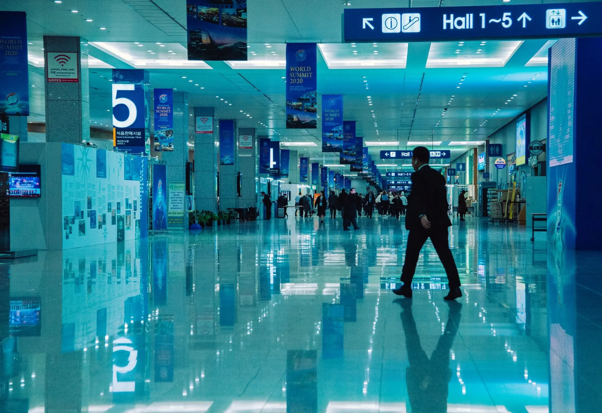 A large exhibition hall lit in blue with a single figure walking through it